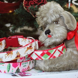 K&ouml;nnte beinhalten: Drei festliche Hundehalsb&auml;nder mit Weihnachtsmotiven. Die Halsb&auml;nder sind rot, wei&szlig; und gr&uuml;n mit Rentier-, Ornament- und Karomustern. Ein pl&uuml;schiger grauer Spielzeughund liegt auf den Halsb&auml;ndern.