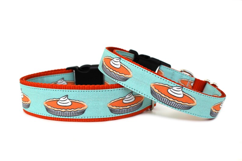 May include: Two dog collars with a turquoise background and a pattern of orange pumpkin pies with white whipped cream on top. The collars are red on the inside and have black buckles.