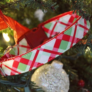 K&ouml;nnte beinhalten: Roter, gr&uuml;ner und wei&szlig;er karierter Hundehalsband mit einer silbernen Schnalle. Das Halsband h&auml;ngt an einem Weihnachtsbaum.
