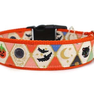Peut inclure: Un collier pour animal de compagnie orange avec un motif répétitif en losanges illustré de symboles d'Halloween comme des citrouilles, des boules de cristal, des chauves-souris, des lunes et des chats noirs, avec une boucle en plastique.