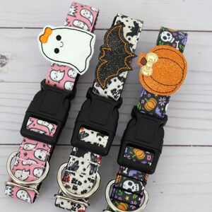 May include: Three Halloween-themed dog collars. One is pink with ghost patterns and a ghost applique. The second is black and white with a bat applique. The third is purple with pumpkin and skull patterns and a pumpkin applique. Each has a black buckle.