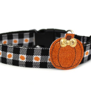 May include: Black and white plaid dog collar with orange pumpkin accents. The collar features a black plastic buckle and a decorative orange glitter pumpkin charm with a gold bow. A festive accessory for pets.