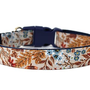 May include: A beige dog collar with a floral pattern featuring blue, orange, and brown flowers. The collar has a navy blue adjustable buckle.
