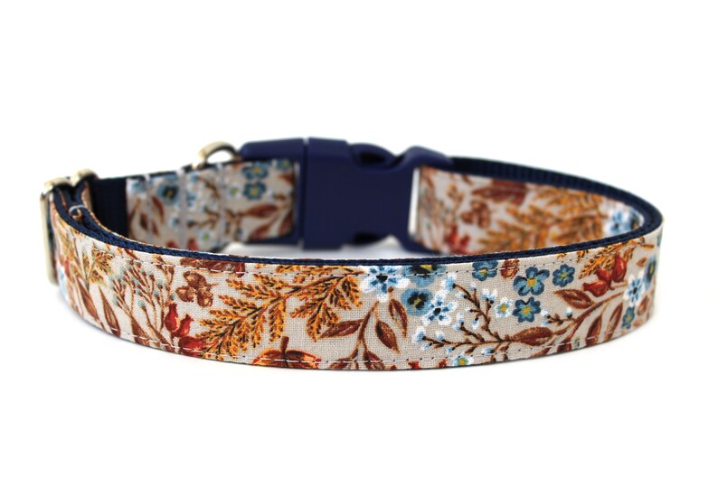 May include: A beige dog collar with a floral pattern featuring blue, orange, and brown flowers. The collar has a navy blue adjustable buckle.