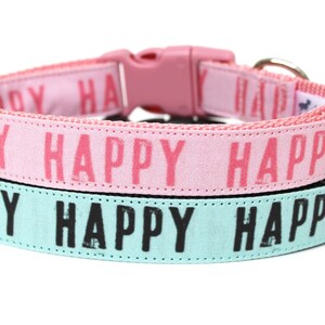 May include: Two dog collars with the word "Happy" repeated on each. The top collar is pink with pink lettering and the bottom collar is light blue with black lettering.