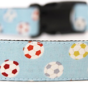 Peut inclure: Un collier pour chien bleu clair avec un motif r&eacute;p&eacute;t&eacute; de ballons de football color&eacute;s. Le collier a une boucle en plastique noire.