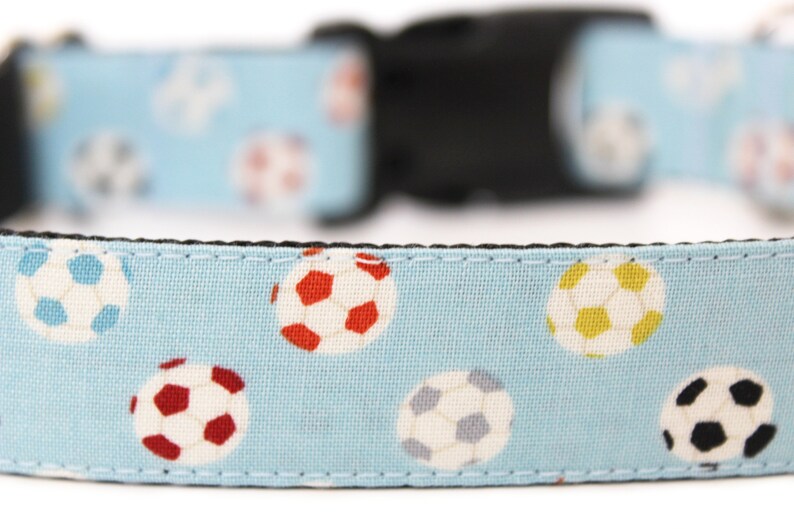Peut inclure: Un collier pour chien bleu clair avec un motif r&eacute;p&eacute;t&eacute; de ballons de football color&eacute;s. Le collier a une boucle en plastique noire.