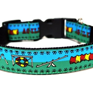 May include: A dog collar with a black buckle and a blue and green pattern. The pattern includes agility course obstacles, paw prints, and the word "AGILITY". The collar is designed for dogs.