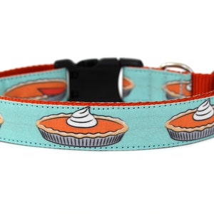 May include: A turquoise blue dog collar with a red trim and a repeating pattern of pumpkin pies with whipped cream on top.