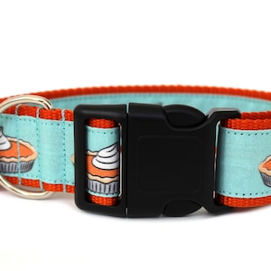 May include: A turquoise blue dog collar with orange trim and a black buckle. The collar features a repeating pattern of pumpkin pie slices with whipped cream.