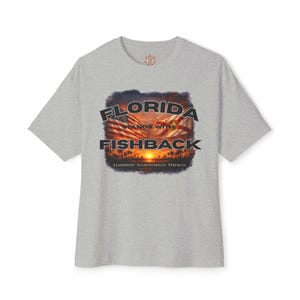 May include: A light gray t-shirt featuring a graphic with the text "FLORIDA STANDS WITH FISHBACK" above a sunset scene with palm trees and the Florida state flag. The text "LEADERSHIP. ACCOUNTABILITY. STRENGTH." is below the graphic.