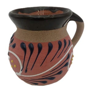 May include: A handcrafted ceramic mug with a handle. The mug features a reddish-pink body with white and dark blue floral designs. The rim is dark brown, and the handle is tan. Yellow dots accent the design.