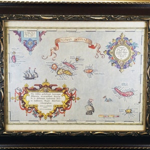 May include: Framed vintage map of the Azores Islands, featuring detailed illustrations of the islands, ships, and decorative cartouches. The map is in a dark brown wooden frame with gold accents, creating a classic aesthetic.