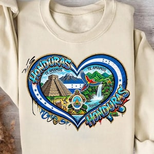 May include: Cream-colored sweatshirt featuring a heart-shaped design with the word "Honduras" in graffiti style. The heart contains images of a pyramid, waterfall, parrot, and the text "Te Amamos".