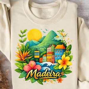 Puede incluir: Sudadera color crema con un gráfico colorido de Madeira. El diseño incluye un sol amarillo, montañas verdes, edificios, flores y la palabra "Madeira" en escritura amarilla. También se ve un teleférico.