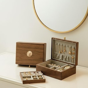 Könnte beinhalten: Dunkelbraune Holzschmuckkästchen in verschiedenen Größen, einige geöffnet, andere geschlossen. Eine Box hat ein goldenes Medaillon. Die geöffneten Kästchen zeigen Fächer und Schmuck, darunter Halsketten und Ringe.