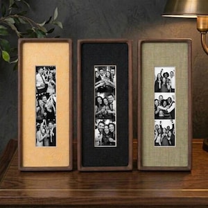 May include: Three vertical rectangular photo frames with dark wood borders. The left frame has a textured yellow mat, the center frame has a black mat, and the right frame has a textured olive green mat. Each frame displays three stacked black and white photos.