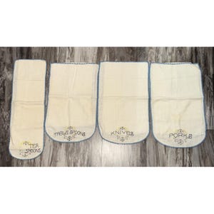 May include: Four off-white linen kitchen utensil holders with blue trim. Each holder is labeled with embroidered text: "TEA SPOONS", "TABLE SPOONS", "KNIVES", and "FORKS". Floral embroidery accents the text.