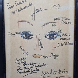 Op de afbeelding: Een ingelijste make-upschets uit 1987, met een gestileerd gezicht met gedetailleerde instructies voor oogmake-up. De schets bevat kleurnamen als "Silver Blue", "Honey Gold" en "Texas Poppy", samen met de handtekening van de kunstenaar.