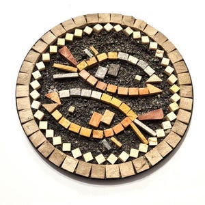Pode incluir: Uma obra de arte em mosaico redondo com dois peixes voltados um para o outro. Os peixes são feitos de várias telhas coloridas, incluindo laranja, cinza e bege, contra um fundo escuro. A borda é feita de pequenas telhas quadradas.