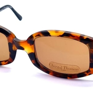 May include: Tortoiseshell sunglasses with brown lenses. The frames have a rectangular shape with decorative black metal arms. The lenses have a slight tint, and the brand name "Chantal Thomass" is visible on one lens.