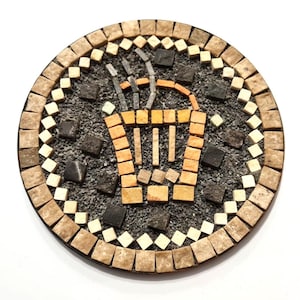 Pode incluir: Base redonda de mosaico com um desenho de xícara de café. A base tem uma borda de azulejos bege e creme. A xícara de café é feita de azulejos laranja e bege, com vapor subindo. O fundo é cinza escuro.