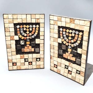 Pode incluir: Dois suportes de livros em mosaico. Cada suporte de livros apresenta um design retangular com uma menorá de mosaico no centro. O mosaico é feito de pequenas telhas quadradas em tons de bege, castanho e preto. Os suportes de livros têm uma base de metal.