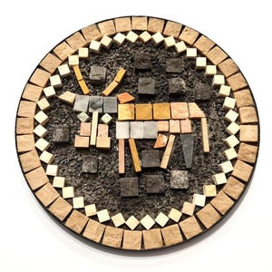 Pode incluir: Uma obra de arte em mosaico redondo com uma figura de animal estilizada. O mosaico é composto por várias telhas de pedra coloridas, incluindo bege, castanho, cinza e laranja, sobre um fundo cinza escuro. A borda é feita de telhas quadradas.