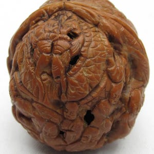 Puede incluir: Una esfera tallada marrón detallada con intrincados patrones en relieve. La superficie presenta un diseño complejo con múltiples figuras y texturas, y varios agujeros pequeños. La apariencia general sugiere un objeto decorativo hecho a mano.
