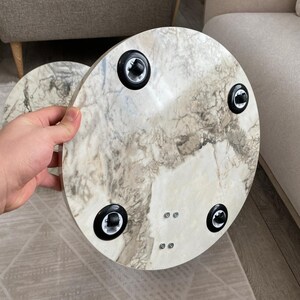 Op de afbeelding: Een ronde tafel met een wit en grijs marmerpatroon. De onderkant van de tafel heeft zwarte poten. De tafel heeft een diameter van ongeveer 40 cm. De achtergrond is neutraal.