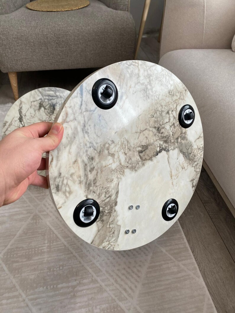 Op de afbeelding: Een ronde tafel met een wit en grijs marmerpatroon. De onderkant van de tafel heeft zwarte poten. De tafel heeft een diameter van ongeveer 40 cm. De achtergrond is neutraal.