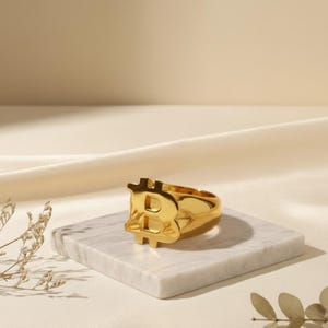 Könnte beinhalten: Eine weiße Keramik-Tasse mit schwarzem Henkel und dem Text "But First, Coffee" in schwarzer, fetter Schrift. Die Tasse steht auf einer weißen Oberfläche. Die Tasse ist etwa 10 cm hoch.