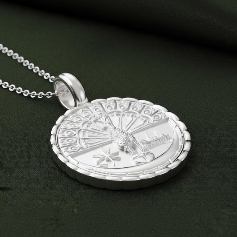 May include: A silver pendant necklace featuring a detailed peacock design. The round pendant has an intricate border and a detailed peacock in the center. The necklace is on a silver chain, and the background is a dark green.