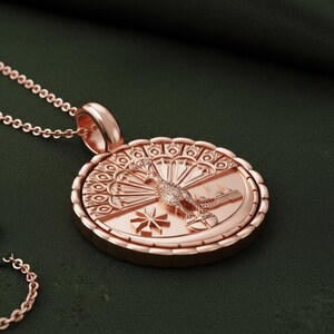May include: Rose gold pendant necklace featuring a detailed circular pendant. The pendant showcases a bird, a building, and a starburst design. The necklace has a delicate chain and a matching rose gold clasp.