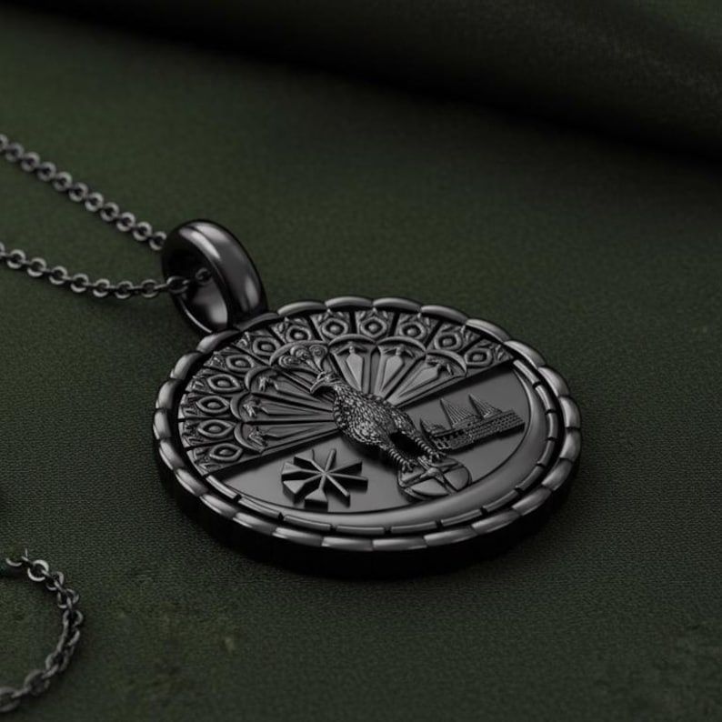 May include: A black pendant necklace featuring an oval-shaped pendant with a detailed design. The pendant showcases a bird with a fanned tail, a building, and a starburst design. The necklace chain is also black.