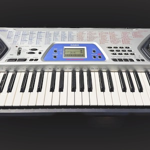 May include: Silver and black Casio CTK-491 keyboard with white and black keys. The keyboard has two built-in speakers, a blue display screen, and various function buttons. The model name is visible on the right side.