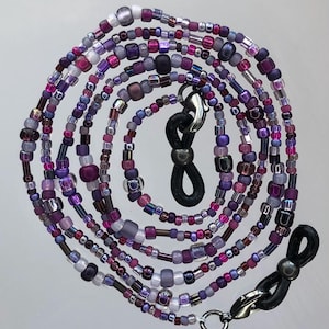 May include: A multi-strand beaded eyeglass chain with purple, pink, and white beads. The chain has two black rubber loops with silver metal clasps.