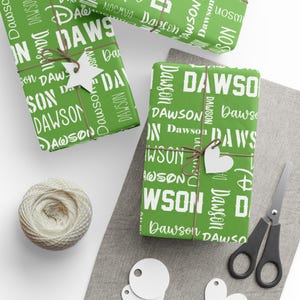 May include: Gifts wrapped in green paper printed with the name "Dawson" in white. The presents are tied with twine and decorated with heart and star-shaped tags. A ball of twine, scissors, and blank tags are also present.