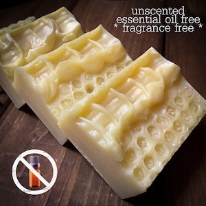 May include: Three bars of unscented, essential oil free, and fragrance free soap. The soap is a light yellow color and has a honeycomb pattern on the top. The bars are rectangular and sit on a dark wooden surface.
