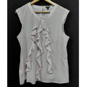 May include: A sleeveless light lavender blouse featuring a round neckline and a vertical ruffled panel down the center front. The garment has a smooth, solid-colored fabric construction with a small black label at the inner neck area.