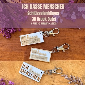 May include: Three keychains with the German phrase "ICH HASSE MENSCHEN" (I hate people) in a stylized font. The keychains are white with gold-colored text and silver-tone clasps. The image also includes text: "Schlüsselanhänger 3D Druck Datei 6 FILES 3 VARIANTS 2 SIZES."