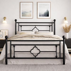 May include: A black metal bed frame with a decorative quatrefoil design on the headboard and footboard. The bed is made up with white bedding and a beige blanket. Two framed landscape prints hang above the bed.