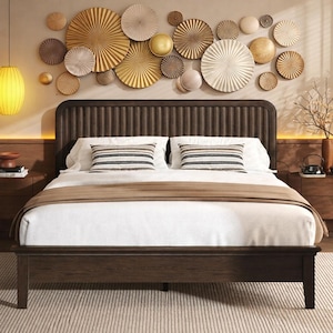 May include: A dark brown wooden bed frame with a matching headboard. The bed is made with white bedding and a brown throw blanket. Two decorative pillows with horizontal stripes are on the bed. The wall behind the bed has decorative paper fans in gold, white, and brown.