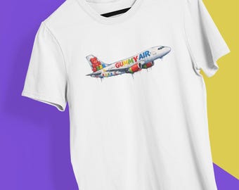 May include: White t-shirt featuring a colorful illustration of an airplane with the text "GUMMY AIR." The airplane design includes gummy bear details and dripping paint effects, creating a playful and vibrant aesthetic.