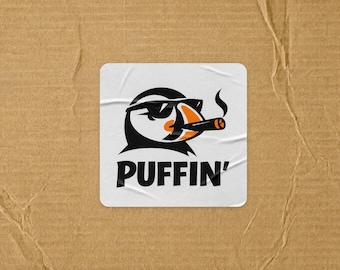 May include: A square white sticker featuring a black and orange graphic of a puffin wearing sunglasses and smoking a cigar. The text PUFFIN' is printed in bold black capital letters below the illustration. The sticker has a slightly wrinkled texture.