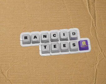 May include: A sticker featuring a collection of light gray computer keyboard keys arranged to spell out RANCID TEES, with a final purple key displaying a yellow R and the text RANCID TEES in a smaller font, all on a white die-cut backing.