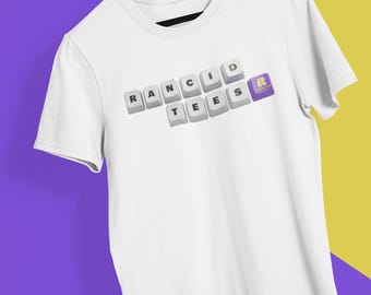 May include: White t-shirt with the text "RANCID TEES" in a keyboard key design. The letter "R" is a purple keyboard key. The shirt is hanging on a wooden hanger against a purple and yellow background.