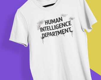 May include: White t-shirt with the text "HUMAN INTELLIGENCE DEPARTMENT" in black, with a distressed, spray-paint style design. The shirt is hanging on a wooden hanger against a purple and yellow background.
