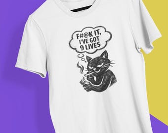 May include: White t-shirt with a black graphic of a smoking cat and the text "F#@K IT, I'VE GOT 9 LIVES" in a thought bubble. The shirt is hanging on a wooden hanger.