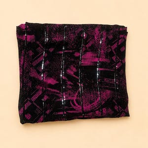 May include: A folded rectangular fabric piece featuring a black base with a vibrant magenta abstract brushstroke pattern. The textile is accented with vertical rows of small, reflective silver sequins that run across the length of the fabric.